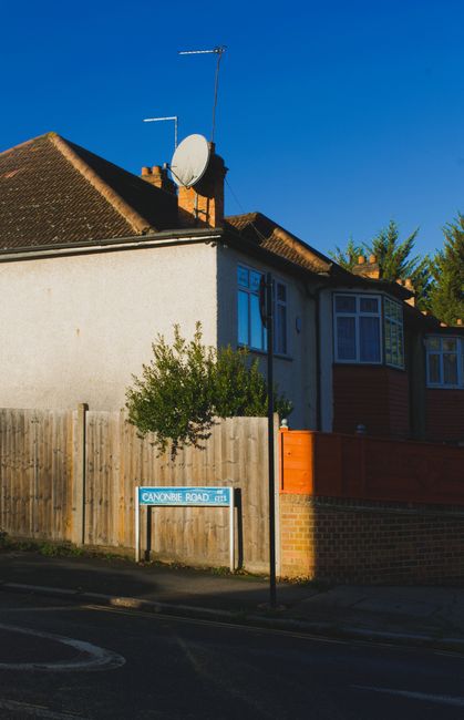 A street scene in Winchmore Hill showing a row of multi-storey residential buildings with brick facades, gabled roofs, and bay windows, situated along the pavement on a clear day with a blue sky and s