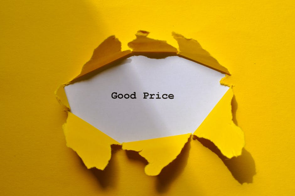 A close-up photograph of a yellow paper surface with a torn hole revealing a white inner layer. Inside the hole, a handwritten note on white paper displays the words 'Good Price' in black typewriter-style font. The torn edges of the yellow paper are irregular and curled outward, creating a textured frame around the note. The background showcases a flat, smooth yellow area, and the lighting is even, highlighting the torn paper's texture and shadows cast by the edges. The scene suggests an emphasis on affordability or value, linked to house removals or moving services, with the torn paper and note implying a focus on cost-effective furniture transport or packing solutions provided by [COMPANY_NAME], consistent with content about understanding removal estimates and pricing in Winchmore Hill.