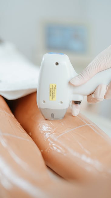 Close-up image showing a professional using a handheld ultrasound device to examine a person's thigh during a medical assessment, with the patient's leg covered in a transparent gel. The background includes a partially visible monitor displaying diagnostic information. The scene takes place in a clinical environment, demonstrating medical imaging technology relevant to health checks, which could relate to health considerations during house removals or relocation processes managed by Man with Van Winchmore Hill. The focus is on the practitioner's gloved hand holding the ultrasound probe against the patient's skin, highlighting the detailed positioning necessary for accurate imaging. The setting is well-lit, emphasizing the technical equipment and the ongoing diagnostic procedure in a professional healthcare context, with the image supporting themes of thoroughness and care in service processes.